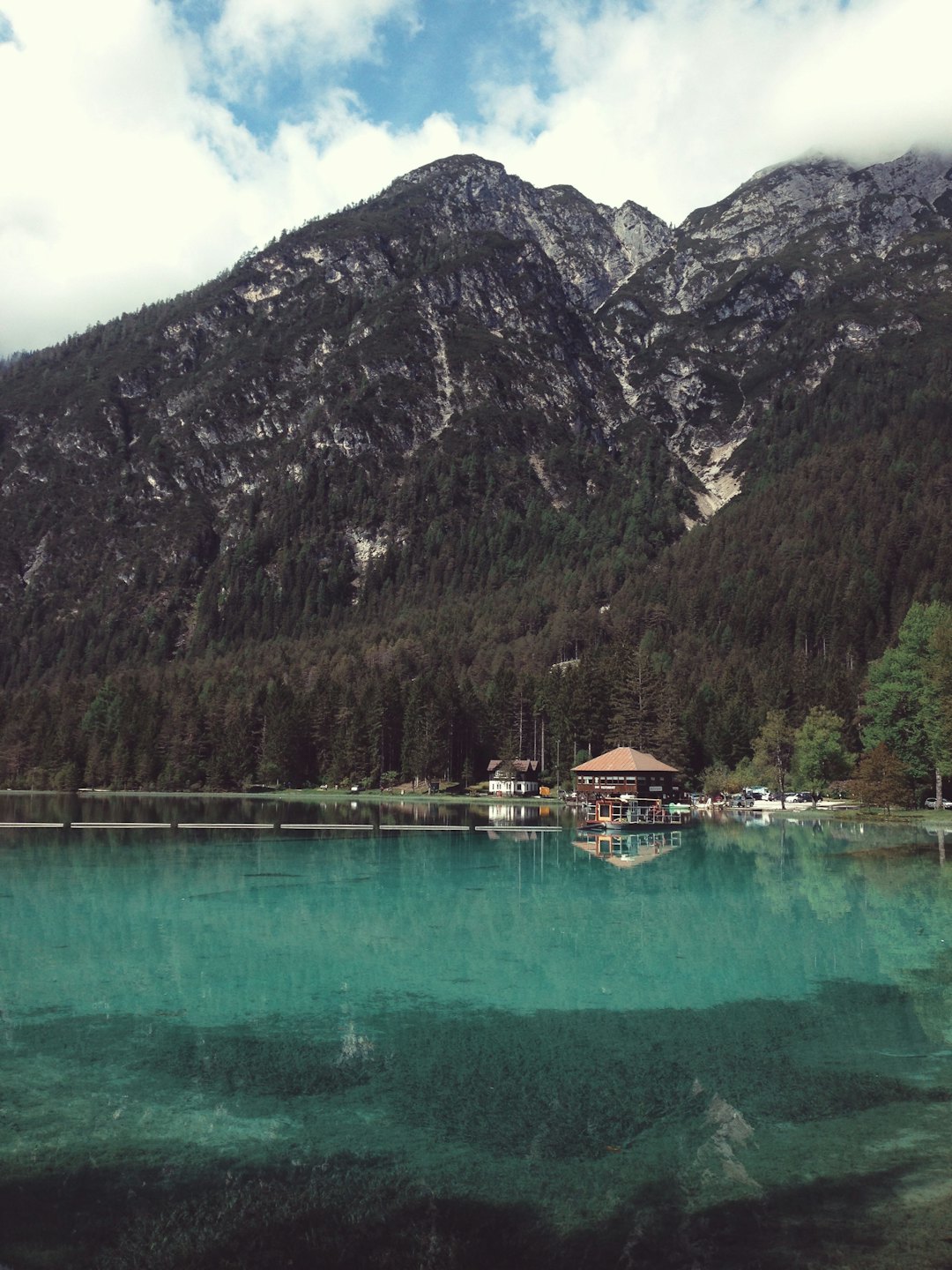 Türkiser See spiegelt Kiefernwald und Berge nahe einer Hütte.