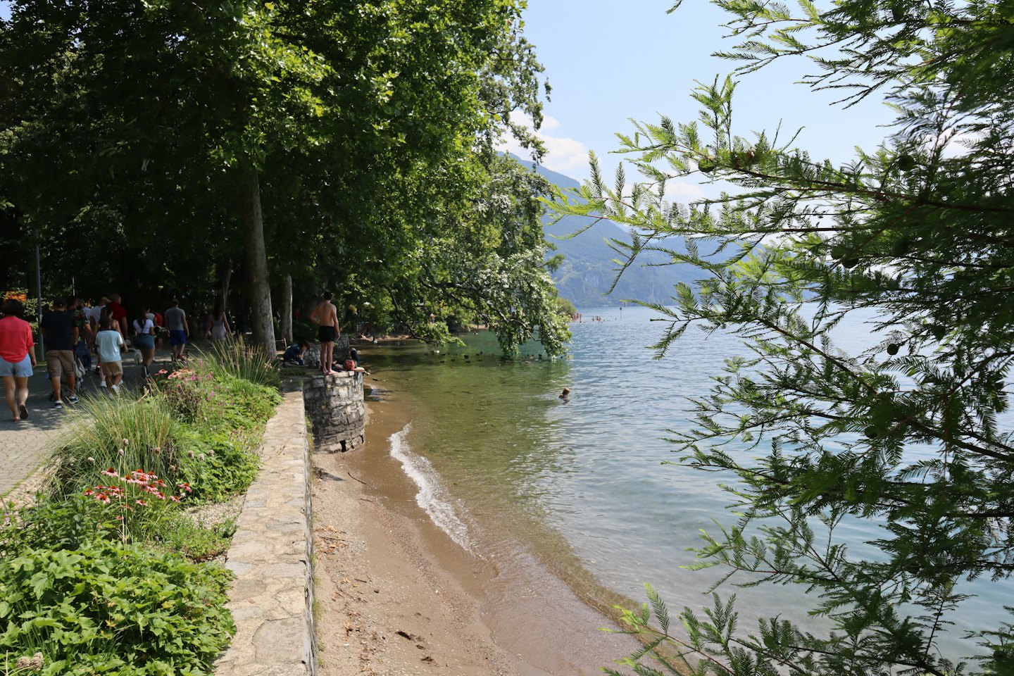Menschen spazieren und entspannen sich auf einem Uferweg mit Bergen in der Nähe.